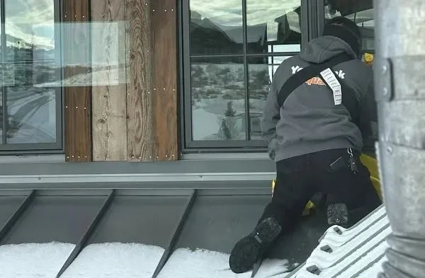 Crew member cleaning an exterior roof edge in the snow