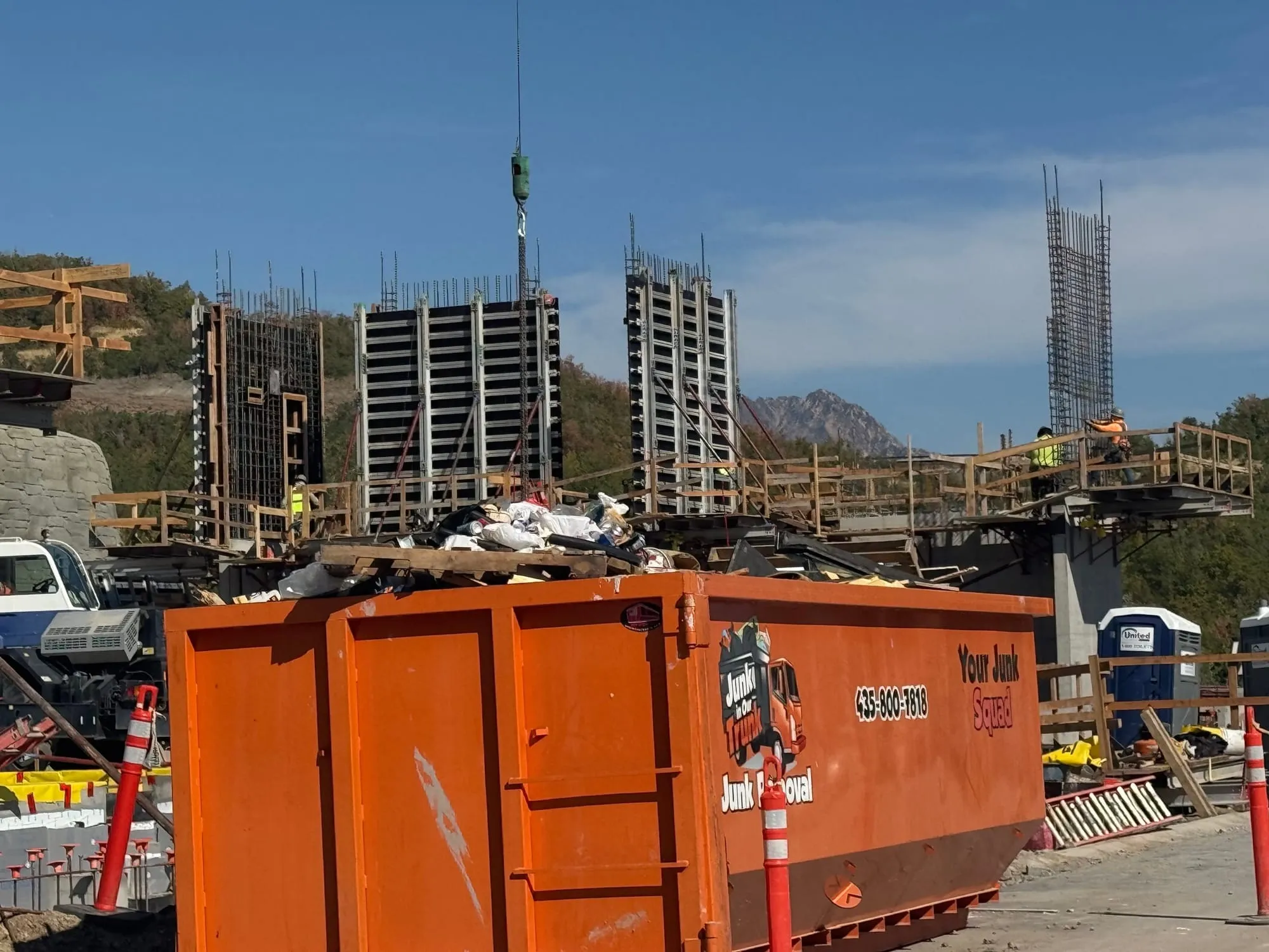 Full orange dumpster at a large commercial concrete build with a crane