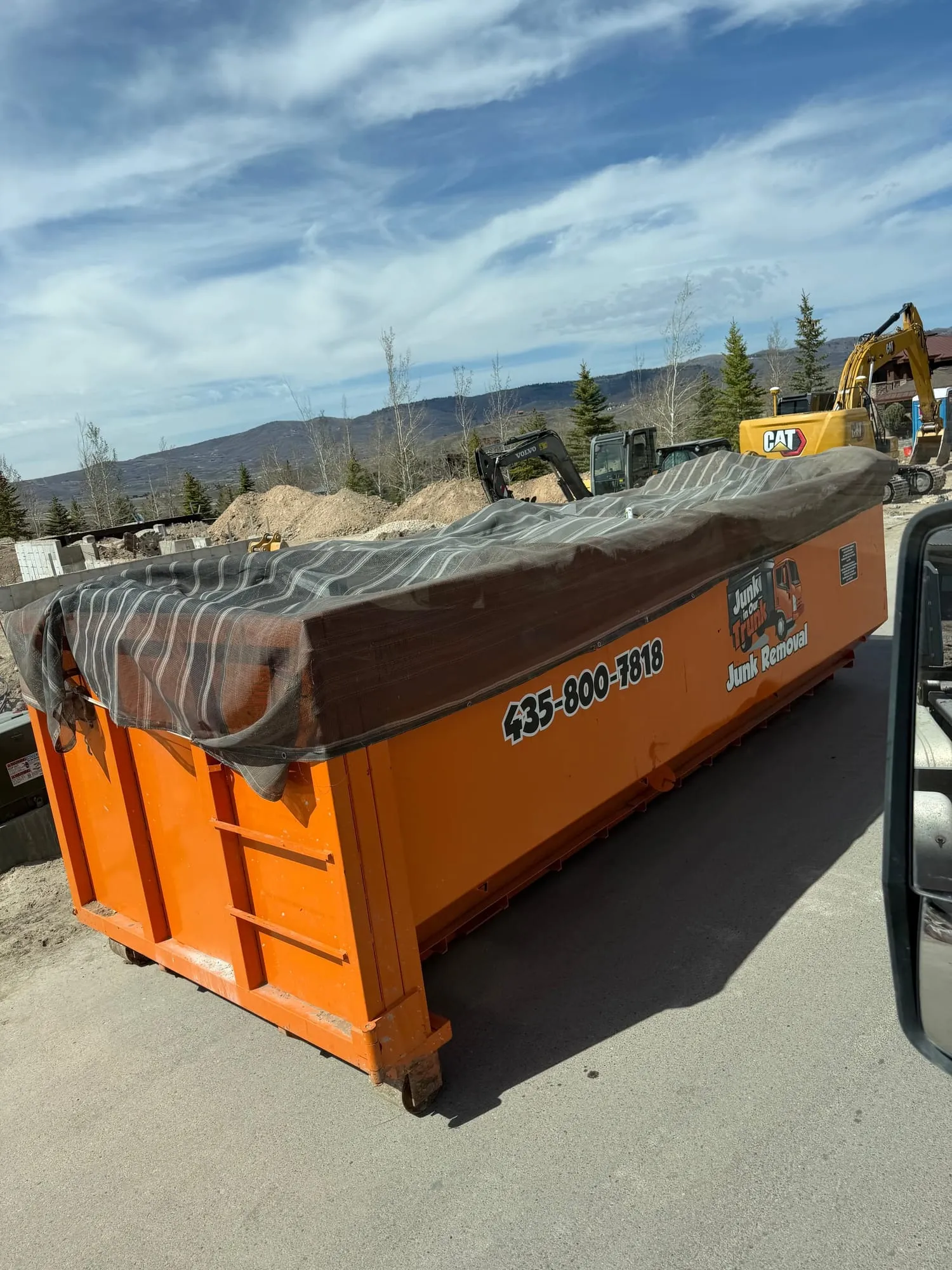 Tarped orange dumpster beside an excavator