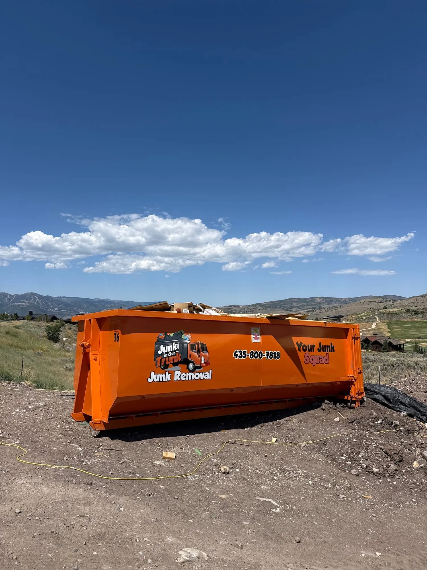 Loaded orange dumpster on a hillside jobsite with mountain views