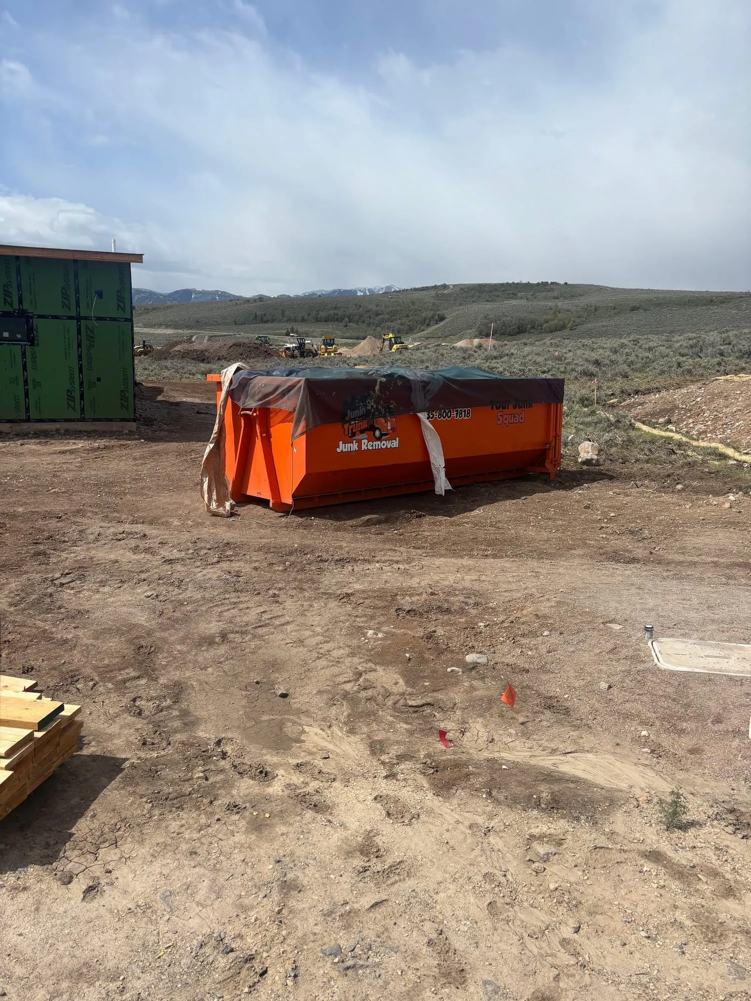 Tarped dumpster on an open lot with snowy peaks behind