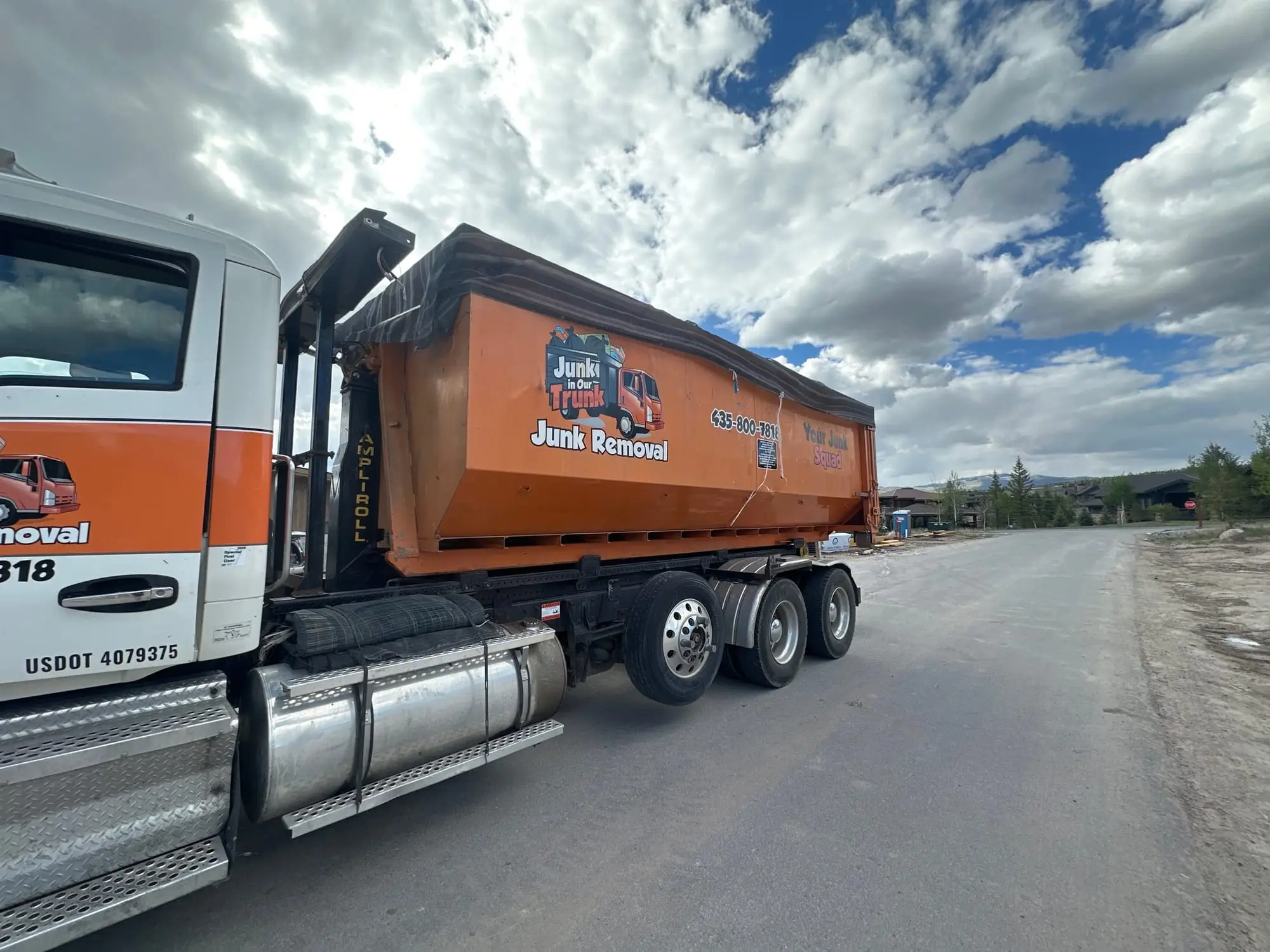 Junk In Our Trunk roll-off truck hauling an orange dumpster