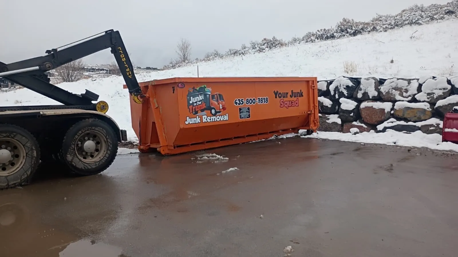 Truck setting a dumpster beside a snowy rock wall